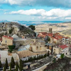 Vista aérea de un pueblo de casas de piedra con tejados rojos, anidado en la ladera de la roca del corb, bajo un cielo azul con nubes.