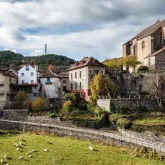 Casas de piedra y tejados rojos se asoman en el **valle de Ansó**, con ovejas pastando en un prado verde y un cielo nublado.