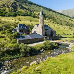 El santuari de Montgarri, una joya arquitectónica de piedra, se alza sereno junto a un arroyo cristalino, rodeado de verdes laderas montañosas.