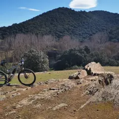 Bicicleta de montaña lista para explorar las **rutas en bici de montaña** en un paisaje rocoso y boscoso bajo un cielo azul.
