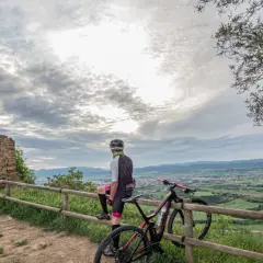 Ciclista descansa junto a su bici en ruinas de coll sa cabra, contemplando el valle.