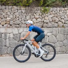 Ciclista pedaleando por una carretera en Mallorca en bici, con un muro de piedra detrás.