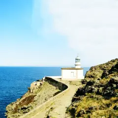 El faro de Cala Nans se alza sobre un acantilado rocoso, vigilando el azul intenso del mar Mediterráneo bajo un cielo despejado.
