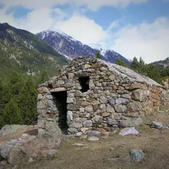 Antigua cabaña de piedra en el Vall de la Llosa, rodeada de pinos y montañas nevadas.