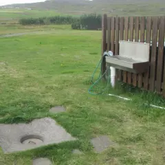 Zona de vaciado de aguas negras para caravana. Un lavabo y un cubo de basura junto a una valla de madera.