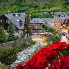 Pueblo pintoresco en el Pirineo Catalán, con casas de piedra y tejados grises junto a un río. Flores rojas en primer plano.