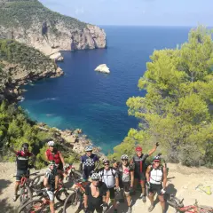 Grupo de ciclistas posa con sus bicicletas en un acantilado con vistas al mar azul. ¡Una aventura en la bicicleta Ibiza!