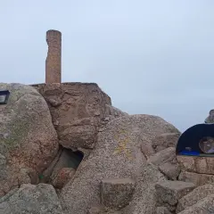 Cima del Puig de Cadiretes con un monolito, rocas y un pequeño refugio con un objeto en su interior.