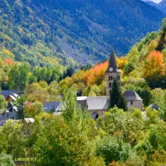Pueblo en el **Valle de Arán** rodeado de árboles con hojas de otoño en tonos verdes, amarillos y naranjas. Destaca una iglesia con campanario.