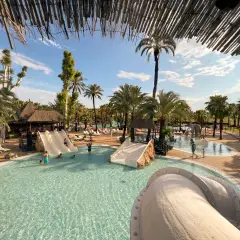 Disfruta de un día soleado en un camping con toboganes en España. Niños y adultos se divierten en la piscina y en los toboganes.