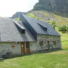 El refugio Vignemale, una construcción de piedra y pizarra, se alza en un prado verde bajo imponentes montañas rocosas.