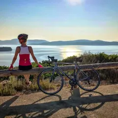 Ciclista descansa tras un tour en bicicleta en Cerdeña, disfrutando de la vista al mar al atardecer.