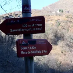 Señales de senderismo en la Vall d'Assua: 300m a Altron y 1,6km a Sorre. El paisaje montañoso y boscoso sugiere una ruta de naturaleza.