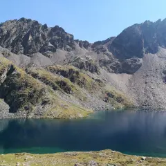 Lago sereno y montañas rocosas cerca del refugi de Baiau.