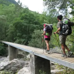 Dos excursionistas con mochilas cruzan un puente de madera en una ruta transpirenaica.