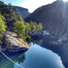 El río fluye sereno en la Foz de Lumbier, rodeado de imponentes rocas y vegetación exuberante bajo un sol radiante.