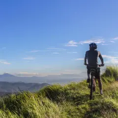 Ciclista en la cima de una colina, disfrutando de las vistas de Galicia en bici. El cielo azul y las montañas de fondo crean un paisaje impresionante.