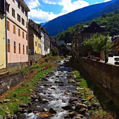 Un río serpentea entre casas de colores y montañas verdes. La **altitud vielha** se siente en el aire fresco y la vista panorámica.