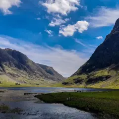 Un paisaje espectacular para hacer **escocia en bicicleta**. Montañas verdes, un lago sereno y un cielo azul con nubes.