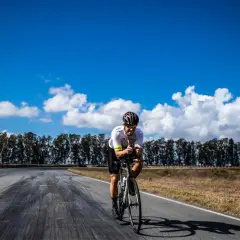 Ciclista pedaleando en la Vía de la Plata en bici, con pulgares arriba bajo un cielo azul y nubes blancas.