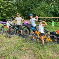 Familia lista para la ruta Pirinexus, con bicicletas y equipaje, disfrutando del paisaje verde.