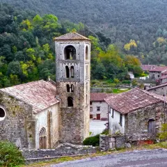 Iglesia románica y casas de piedra en un valle boscoso, ideal para explorar las rutas Camprodon.