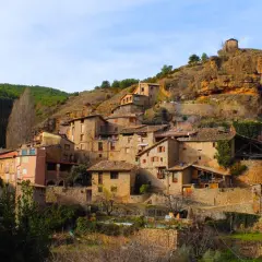 Un pintoresco senet de Barrabés se aferra a la ladera, con casas de piedra y tejados de teja bajo un cielo azul.