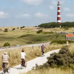 Ciclistas disfrutan de un paseo por la ruta EuroVelo 7, con un faro a rayas rojas y blancas al fondo.