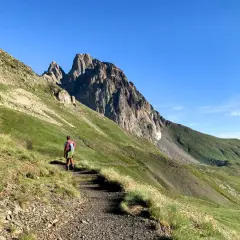 Senderista se dirige hacia el imponente Midi d'Ossau, rodeado de verdes laderas y un cielo azul despejado.