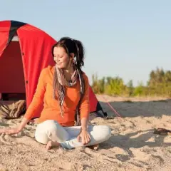 Mujer meditando junto a una tienda roja, disfrutando del acampar en la playa.