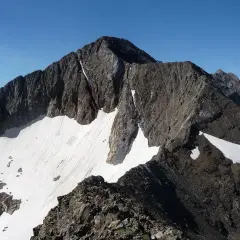 Cumbre rocosa y nevada de un pico posets bajo un cielo azul despejado.