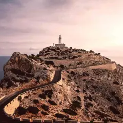Faro en la cima de un acantilado rocoso, con una carretera serpenteante que asciende. Un paisaje de monumentos naturales impresionantes.
