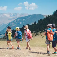 Niños explorando los Pirineos con mochilas, disfrutando de un día soleado con vistas a las montañas y un telesilla.