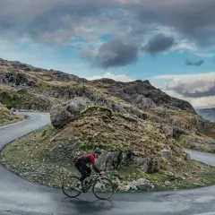 Ciclista en una carretera sinuosa en un paisaje montañoso, disfrutando de su aventura de España en bicicleta.