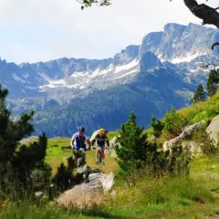 Ciclistas descienden por un sendero en el Pla de Beret, con imponentes montañas nevadas de fondo.