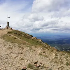 Cima de montaña con cruz y banco, ideal para **rutes per osona**. Paisaje de valles y nubes.