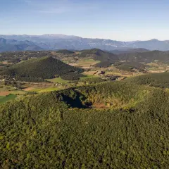 Paisaje aéreo de los volcanes de la Garrotxa, con conos volcánicos cubiertos de vegetación y un cráter visible.