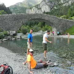 Gente disfrutando del río bajo el puente de piedra en Bujaruelo, con vistas al Taillón.