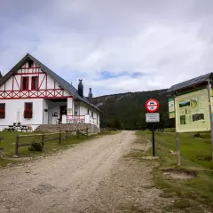 Refugi comes de rubio, un refugio de montaña blanco con detalles rojos, rodeado de pinos y un camino de grava.