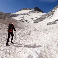 Alpinista asciende por una ladera nevada hacia el pico Aneto, con el cielo azul brillante.