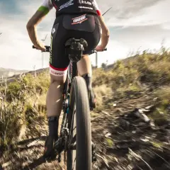 Ciclista desciende por un sendero polvoriento, disfrutando de una de las mejores rutas del mundo en bicicleta. El paisaje árido y las turbinas eólicas al fondo crean una escena épica.
