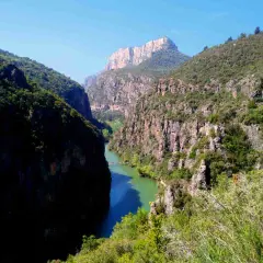 El río serpentea entre imponentes paredes rocosas en el congost del Mu, coronado por un pico montañoso.