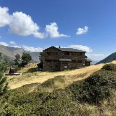 Refugio Comapedrosa, un edificio de piedra en un paisaje montañoso con hierba seca y cielo azul.