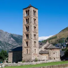 Torre románica de piedra en el Vall de Boí, con montañas y un pueblo al fondo.