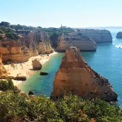 Acantilados dorados y aguas turquesas en una **playa** del **Algarve**. Gente disfrutando del sol y el mar.