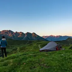 Mujer contempla el amanecer en su acampada libre Francia. Montañas y tienda de campaña en un paisaje idílico.