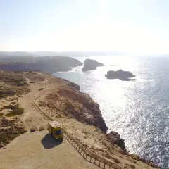 Furgoneta amarilla en un acantilado con vistas al mar, ideal para camping en Algarve, Portugal.