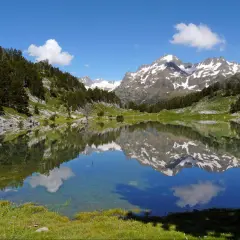 Espejo de agua en los valles de Huesca, reflejando montañas nevadas y un cielo azul con nubes.