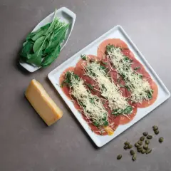 Carpaccio con rúcula y queso rallado, perfecto para llevar en autocaravana. Acompañado de un trozo de queso y alcaparras.