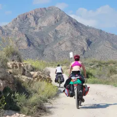 Ciclistas cargados recorren un camino polvoriento bajo un cielo azul, pedaleando por la ruta EuroVelo 8.